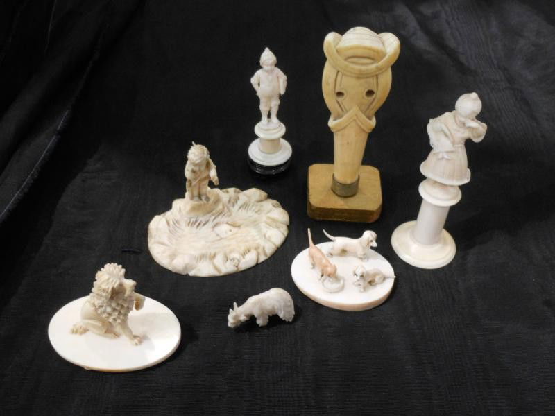SEVEN CONTINENTAL IVORY FIGURINES AND GROUPS: Finely carved miniatures of a crying girl with broken doll standing on pedestal, a school boy carrying book, Cupid with arrows, goat, dog, group of three puppies and parasol handle carved as female po