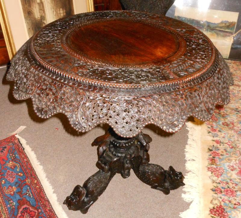 ANGLO-INDIAN 19TH CENTURY TEAKWOOD TILT TOP TABLE: Elaborately carved allover; the circular top with wide band of foliate vines and animals, matching all around pierced apron, the pedestal support of intertwined serpents, and the tripod base showing t