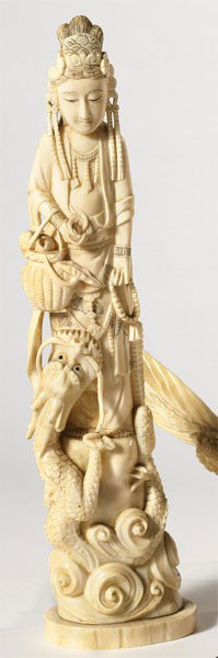 CHINESE IVORY GUAN YIN: Detailed carved tusk in form of a women standing on a rock with crashing waves and emerging dragon, holding a basket of lotus flowers and beaded necklace, 19th/20th century. Height 12 5/8 in.
