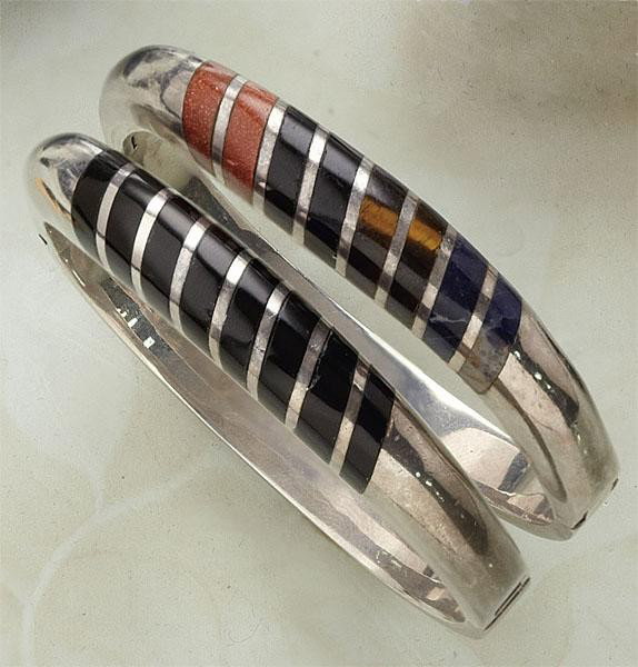 PAIR SILVER BANGLE BRACELETS: Two sterling silver bracelets, one with inlaid onyx stones and one with carnelian, onyx, cats eye, and lapis stones. 93 grams.