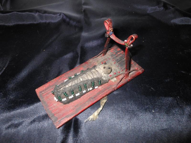 NATIVE AMERICAN WOODLANDS DOLL ON CRADLE BOARD: Probably Ojibwa, the diminutive cloth doll having bead eyes and mouth mounted to red painted bentwood board with beaded decoration. Height 2 1/2 inches, length 4 3/4 inches, width 2 inches.