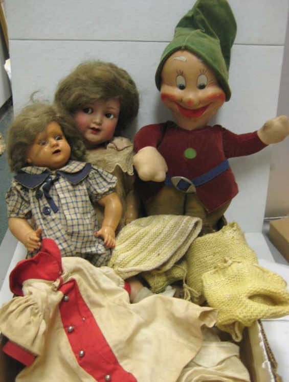 THREE DOLLS: Two German hard plastic and cloth with mask face 'HAPPY'; with two sets of vintage doll clothing.