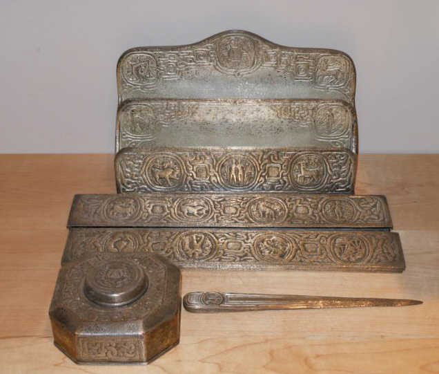 TIFFANY STUDIOS, NEW YORK: ZODIAC DESK SET (five pieces); inkwell, blotter ends, letter tray and letter opener, bronze with rare silver patina, each stamped and numbered. 2 1/4 x 4 1/4 inches (inkwell) 12 1/4 inches (blotter en