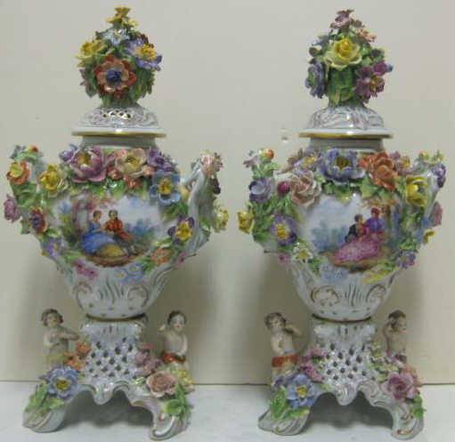 PAIR OF GERMAN PORCELAIN POTPOURRI URNS: Meissen Rococo style, each two handled with applied flowers and painted romantic scene reserves, mounted to pierced bases with seated allegorical children and flowers, covered with pierced lids having