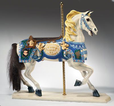 CAROUSEL HORSE: White painted horse is colorfully decorated and bejeweled, carved in to the side is "Designed and Carved by M. Illions", with "HERITAGE" horseshoes.