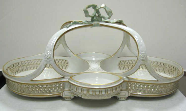KPM, BERLIN, PORCELAIN TWO-DISH BASKET: Footed with cross handle and bow-form finial, each part with openwork sides connected by bridge and two small condiment bowls, gilt highlights, bearing red orb overglaze and blue scepter underglaze ma