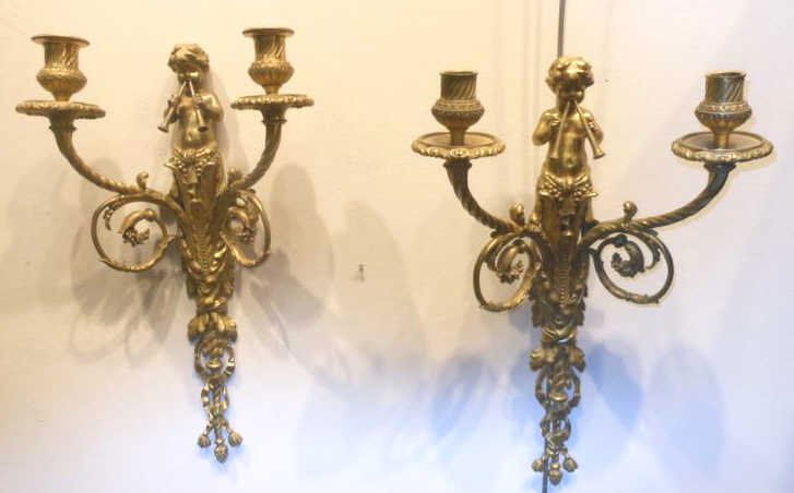SET OF FOUR CONTINENTAL FIGURAL BRASS WALL SCONCES: Elaborately decorated with putti blowing two horns on top, over the scrolling foliate and ribbon decorated drop stems, each with two spiraling arm candle holders. Height 18 1/2 in.
