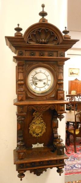 CONTINENTAL 19TH CENTURY REGULATOR WALL CLOCK: Walnut case with arched and shell carved crest, over the circular gilt metal and white enamel dial, above the open shelved area with elaborate swinging pendulum, drop finials below. Height 38 in.