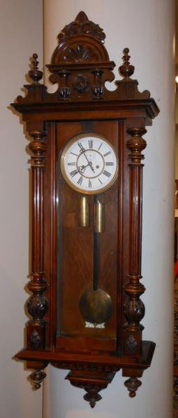 CONTINENTAL REGULATOR WALL CLOCK: Scrolling and foliate crest, over the fill length glazed panel door showing the white enamel dial and pendulum, drop finials below. Height 53 1/2 in.