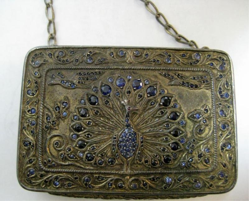 VINTAGE COMPACT: Silver compact with peacock design set with mixed cut faceted round synthetic sapphires. Back is engraved. Inside is gilt with mirror, powder and lipstick case. Compact has chain handle. 3 inches x 2 