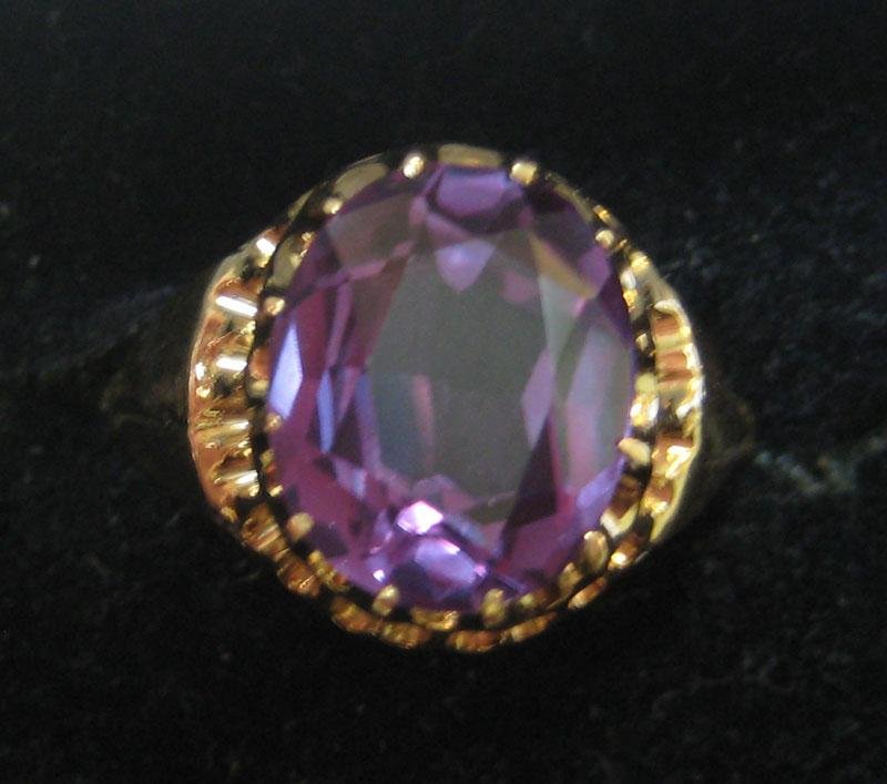 PURPLE COLOR CHANGE RING: 14k yellow gold ring set with one oval faceted synthetic corundum measuring 12mm x 10mm. Ring has an open basket crown. Size 7 1/2. 4.2 grams.