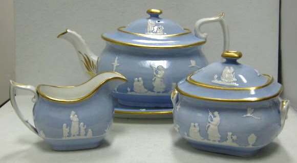 SPODE, STOKE-ON-TRENT, FOUR-PIECE TEASET: Relief figural decoration on pale blue ground, gilt highlights comprising teapot with underplate, sugar bowl and creamer, red SPODE mark, 19th century.