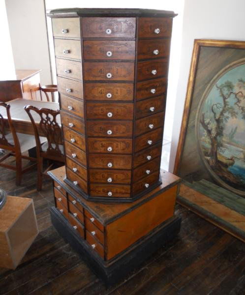 ANTIQUE AMERICAN BOLT BIN: With revolving octagonal 80 drawer top, on the rectangular 18 drawer base, with porcelain handles and ebonized line highlights. Height 67 1/2, width 32, depth 31 in.