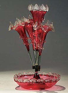 VICTORIAN CRANBERRY GLASS FLOWER EPERGNE: Round bowl issuing a central and three curved trumpet form vases with clear glass petal moulded rims and applied rigaree, circa 1900. Height 19 in., diameter 11 in.