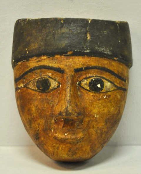 ANCIENT EGYPTIAN FUNERARY MASK: Carved wood bas-relief face with eyes outlined in pigment and face painted in yellow, brown, orange and black, after 600 BC. Height 7 1/2 in., width 6 1/4 in., depth 3 in.