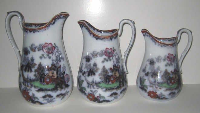 THREE ENGLISH IRONSTONE JUGS, TRANSFER SCENES: A group of jugs graduating in sizes, each with black transfer and painted enamel Chinoiserie landscape and pagoda decoration, 19th century. Heights 9 1/4, 8 1/4 and 7 1/4 in.