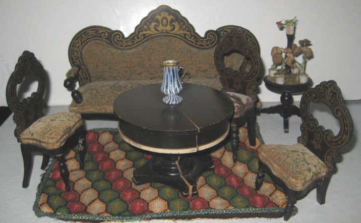 VICTORIAN DOLLHOUSE WOODEN FURNITURE: Gilt decorated, an upholstered sofa with open arms, extendable round pedestal table, three side chairs, tripod urn with flowers, needlework flat weave rug and Italian style art glass pitcher, total 8 