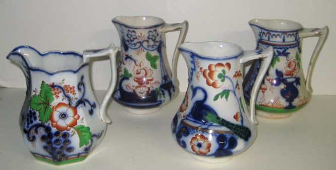 FOUR ENGLISH POTTERY 'GAUDY WELSH' JUGS: Flow blue and polychrome enamel decorated, various floral patterns, one PEACOCK, circa 1840-1870. Heights 7 1/2 in.