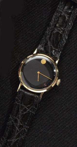 LADY'S GOLD WATCH, MOVADO: 14k yellow gold Museum watch with black dial with signature "dot" at 12:00. Watch has manual wind movement and black leather strap. Running. Box.