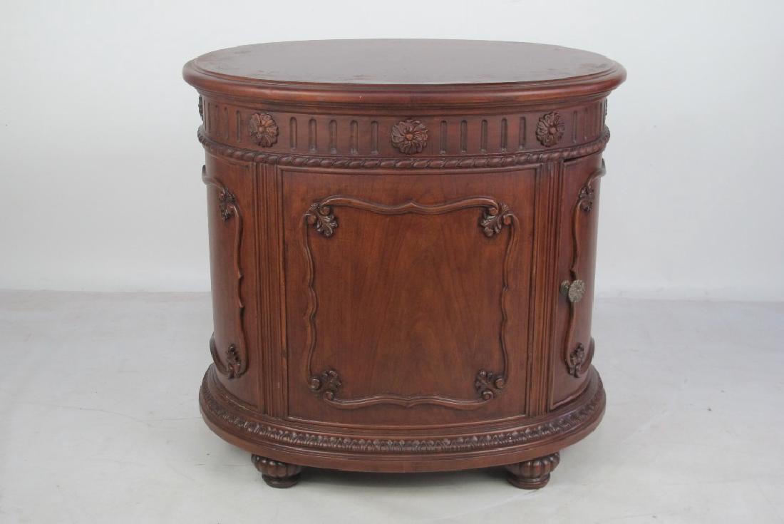 American Drew Commode: Oval form commode having burl detail to top and carved foliate decoration throughout. Door with brass hardware. By American Drew. 27.5 inches height, 30 inches width, 23 inches depth. 27.5"H x 30"W x 