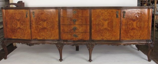 Large Glass Top Burlwood Sideboard: Late 19th - early 20th century. The elongated top is set with a Black glass below and elaborate gilt three-part mirror. The top rest on a base with a center section filled with four drawers between tw