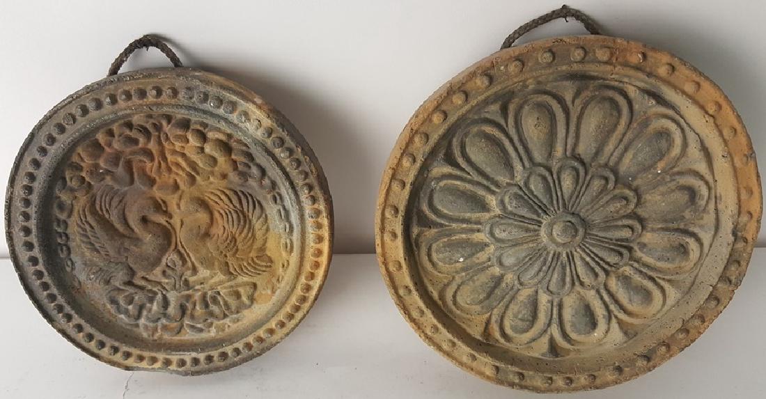Pair of Stone Medallion Wall Hangs: Two circular cast stone medallion wall hangs. One having floral blossom motif and other having symmetrical bird motif. 6 inches diameter. 6" diameter Wear from age and use