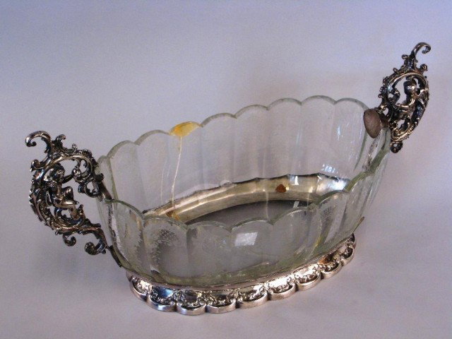 ETCHED GLASS & CONTINENTAL SILVER CENTERPIECE:: With scrolling silver handles, each incorporating a putto, and a silver plate base. Note: Crack to length of piece. 10"H X 18"W