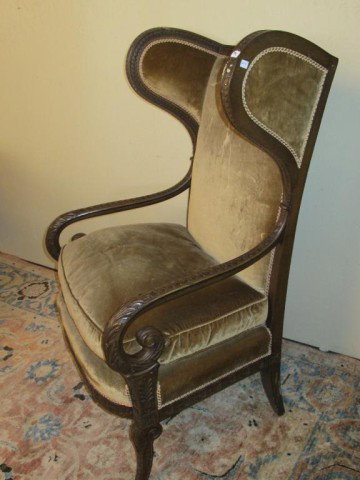 WINGBACK FIRESIDE CHAIR:: Having a finely carved frame with scrolling arms, and soft tan velvet upholstery.