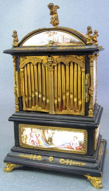 MINIATURE VIENNESE MUSICAL JEWEL CASQUE: Executed in the form of a cabinet organ. The arched top with putti form figures above two bronze doors. All inset with fine enamel plaques depicting various classical landscape, structures, and figure
