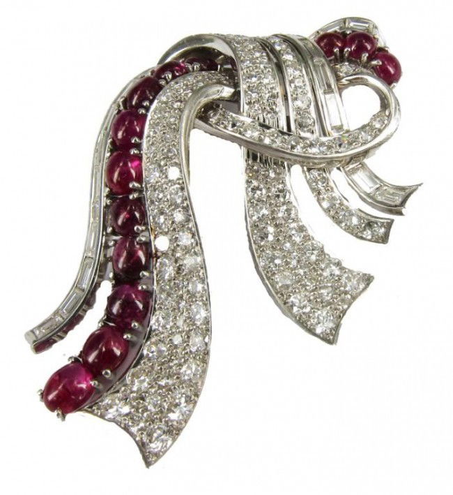 TRABERT HOEFFER MAUBOUSSIN DRESS PIN: Ruby and diamond set in platinum bow form. Set with 13 graduated cabochon rubies, 22 caliber cut diamonds over 9ct diamonds.