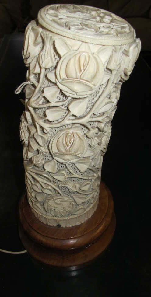 CARVED IVORY TUSK:: An ivory tusk fragment with relief carved leafy vines, flower blossoms and buds on a finely reticulated background, and having a carved ivory circular lid. Mounted on wooden base. Mounted as lamp. Not