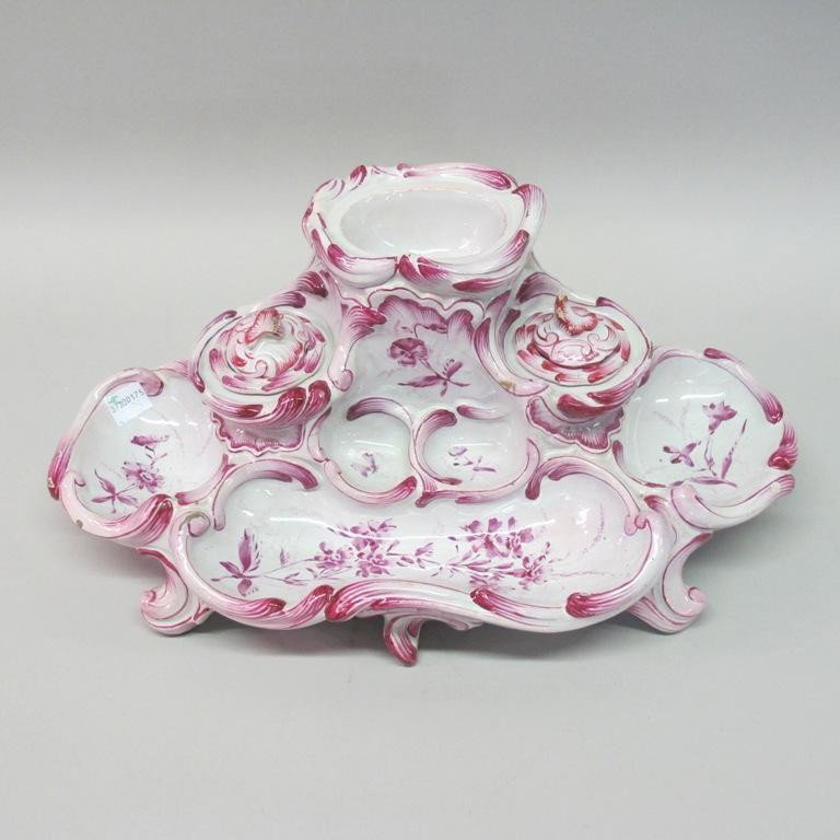 FAIENCE INK WELL: A footed ink well in an undulating form, decorated in white and purple rocaille scrolls and flowers, and having two lidded ink inserts. 6"H X 14.5"W Provenance: The Ferst estate