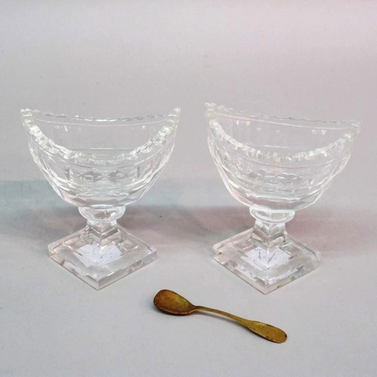 PAIR RAISED CUT GLASS MASTER SALTS.: Boat form glass master salts raised on square feet. Accompanied with 1 sterling spoon. 3.5"H X 3"W Provenance: The Ferst estate