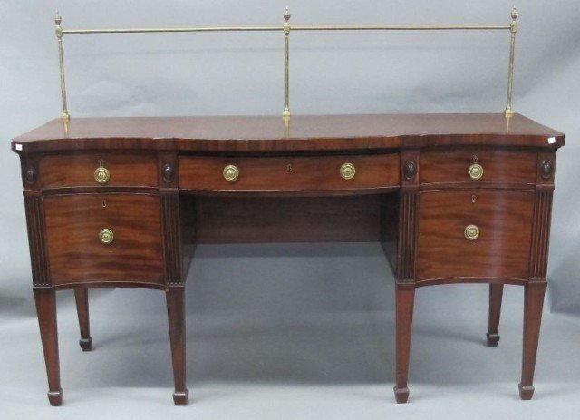 ENGLISH MAHOGANY SIDEBOARD:: A handsome Georgian mahogany sideboard fitted with a convex center drawer flanked by concave drawers with fluted column edges. Having brass posts with urn finials and brass ring pulls. All on tapering
