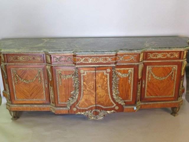 MARBLE TOP BRONZE MOUNTED SIDEBOARD:: A verde antico marble slab surface over a heavily bronze mounted sideboard fitted with three drawers over three cabinets. The center cabinet with two marquetry inlaid doors. All raised on gilt bronze 