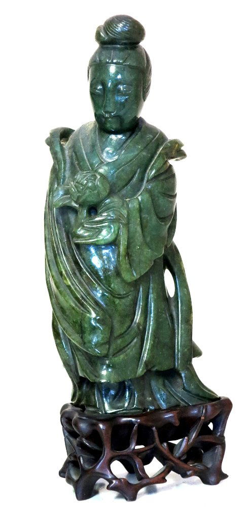 JADE FIGURE OF KUAN YIN: Antique Chinese carved spinach green jade figure of the goddess wearing flowering robes, her high coifed hair dressed with a top knot,; holding in her left hand a peony blossom. Mounted on a custom ca