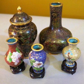 A GROUP OF FIVE CHINESE CLOISONNE VASES:: likely 20th century, comprising an example of bottle form with floral and foliate decoration on a deep red ground together with lidded example of matching decoration of baluster form and three other e