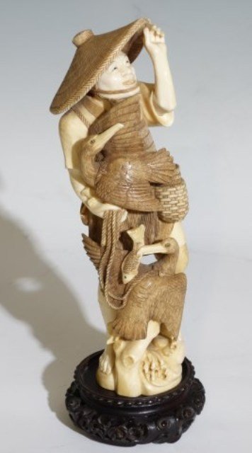 ASIAN IVORY FIGURE FISHERMAN WITH PELICANS: Late 19th / Early 20th century. The man wearing a straw hat accompanied by two captive pelicans. Character marks to base. Along with circular carved wood stand. Figure measures 10 1/2"H
