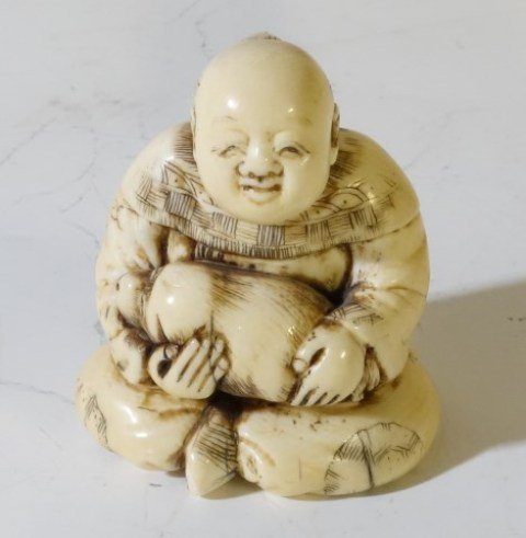 CARVED ASIAN IVORY NETSUKE SEATED MAN: Early 20th century. The carving depicts a seated man holding a dog. 2 1/2"H