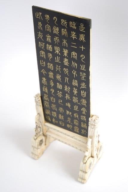 CHINESE SCREEN ON IVORY STAND: 19th century, comprising a stand having incised floral decoration supporting the removable screen depicting a village scene against a pastoral landscape, the reverse with Chinese characters. Overall g