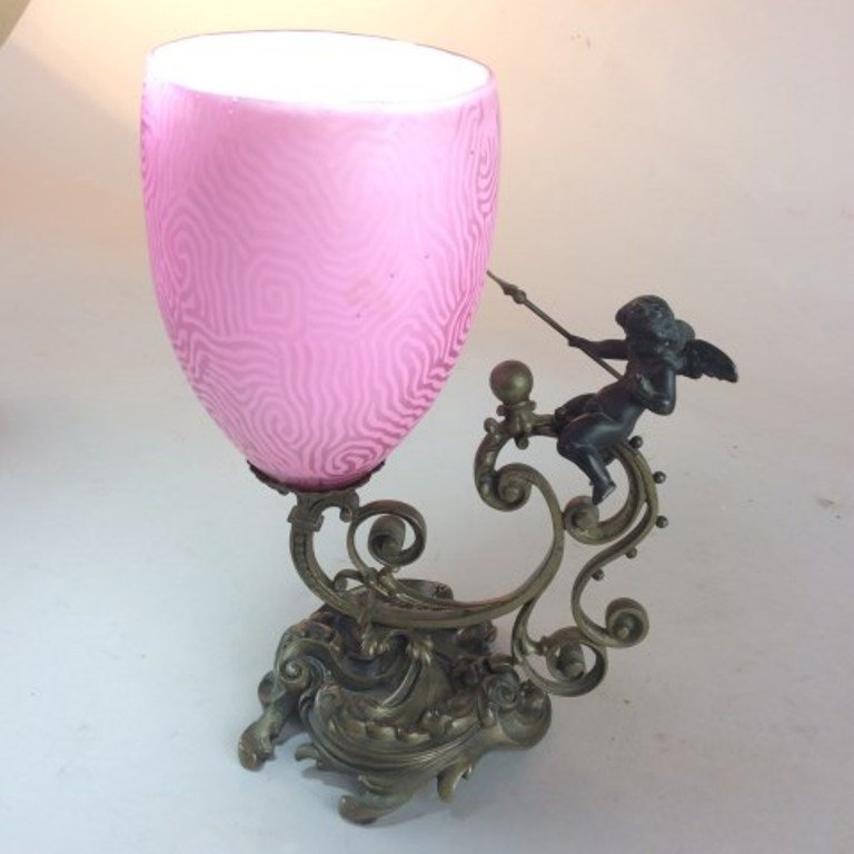VICTORIAN BRONZE AND ART GLASS GARNITURE: The bronze base with a scrolling frame surmounted by a putto with a spear supports a pink satin glass vase with a etched scrolling maze motif. 10"H