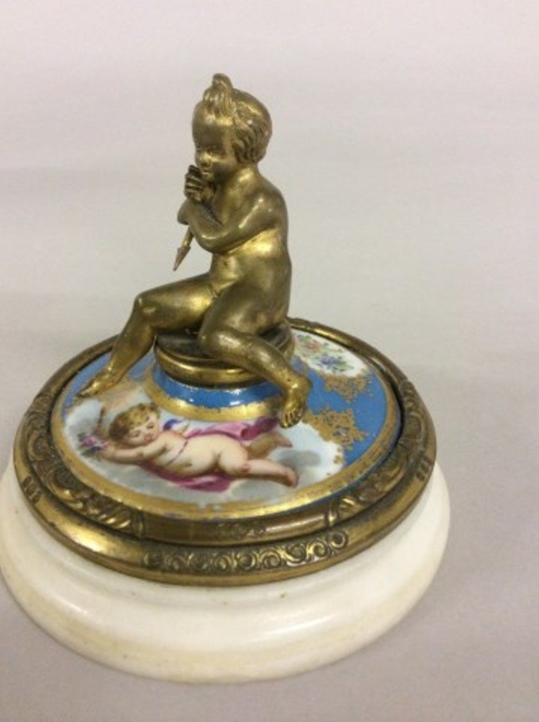 BRONZE PORCELAIN AND MARBLE PAPER WEIGHT: Crested by a gilt bronze figure of a youth holding a spear above painted porcelain band with hand painted floral and putto cartouches on a white circular marble base.
