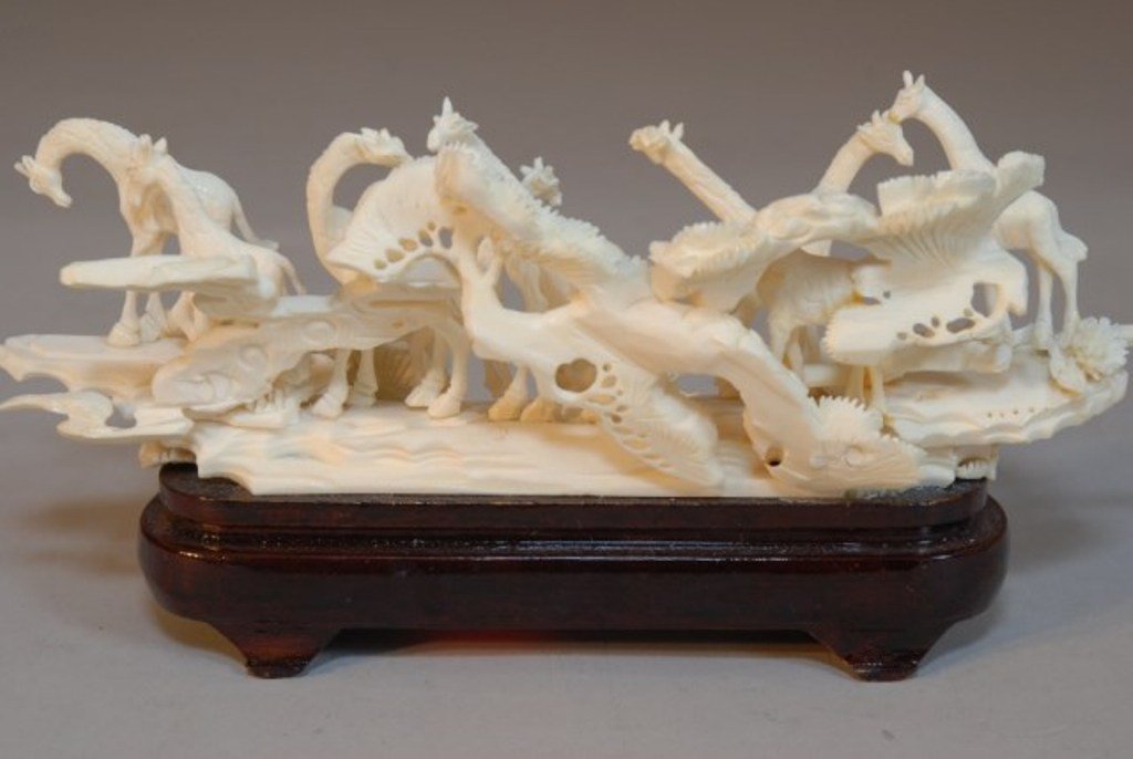 CARVED IVORY FIGURAL GROUP: The elaborate carving depicting a herds of giraffes in a jungle landscape resting on a wooden path. 4"H X 8 1/4" W X 2 1/4" D