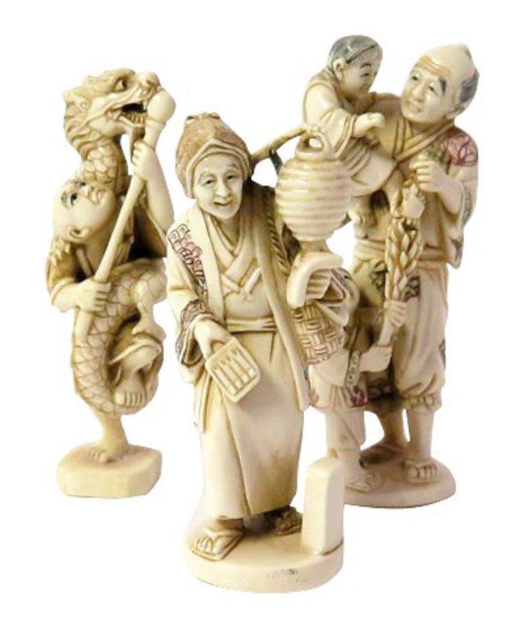 Netsukes Group of Three: A group of three Japanese carved ivory netsukes with partial red ink color. Depicting a merchant, a male figure with two children and a dragon climbing upon a figure holding a staff. Each signed with 