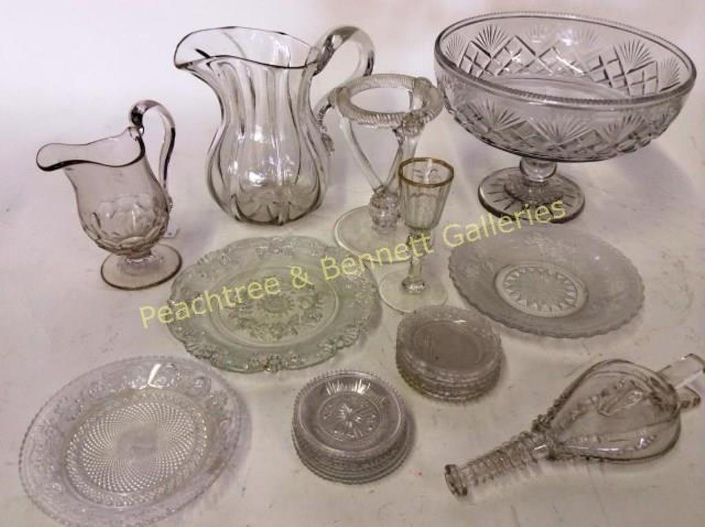 Group Early American Glass: Lot 22 pcs includes 13 glass coasters, 3 small glass plates, 2 pitchers, glass bottle, cordial, glass base and a compote. The largest piece measures: 7" H X 10" D