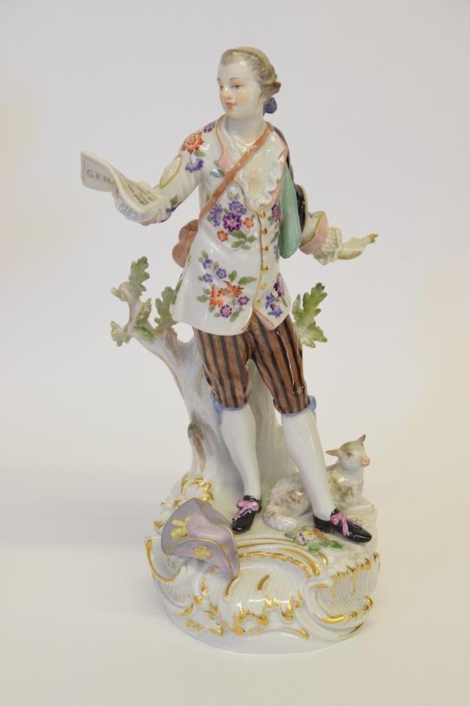 Early 20th Century Meissen Porcelain Figurine: Depicting a man singing from a music sheet held in his right hand. He wears a floral print shirt and a black cloak, a sheep rests at his feet. Marked with Meissen hallmark on the back of the base. Los
