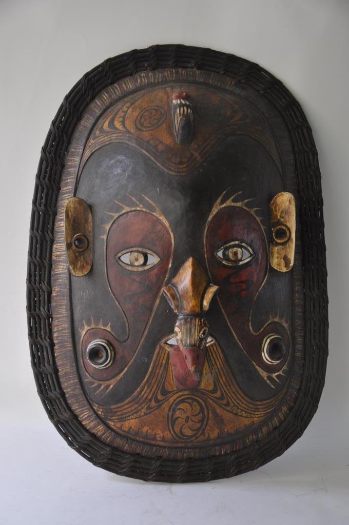 Carved and Painted African Mask: Masked Carved in the shape of a head with a beaky nose shaped like a bird. Mask painted in tribal designs, the whole bordered with a painted rattan. 24 inches height, 17 inches width, 6 inches depth.