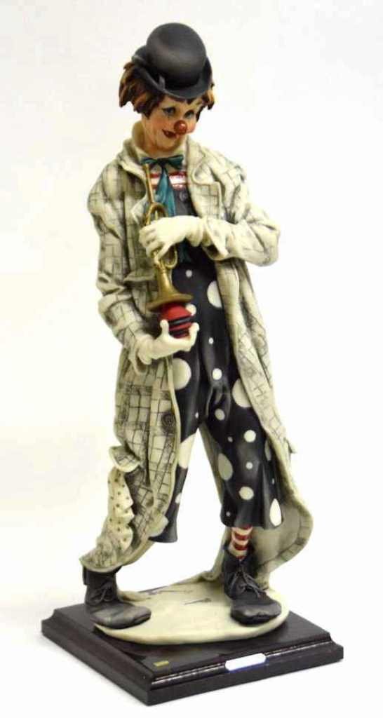 Giuseppe Armani Porcelain Figurine Clown with Trum: Porcelain figurine by Giuseppe Armani in a checked coat over polka dot overalls with bow tie and oversize shoes, holding a trumpet. The whole mounted onto a wooden base with a plaque reading “G. Arm