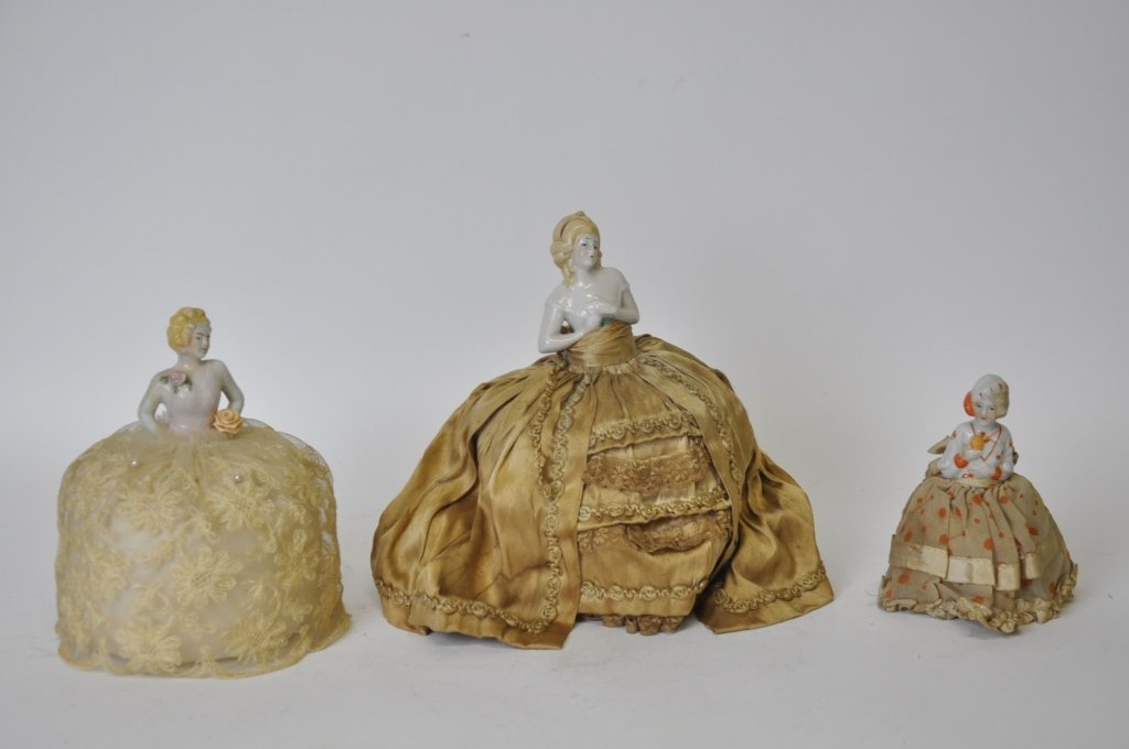 3 Porcelain and Fabric Figurine Pin Cushions: Depicting women, porcelain from the waist up with wire framed fabric skirts. All in good condition. Largest measures 8 inches height, 5 inches diameter. 8"H x 5"Dia 8"H x 5"Dia