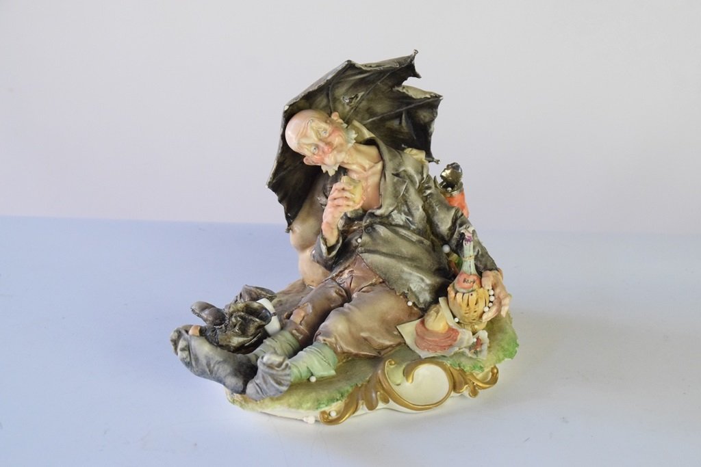 Capodimonte Figure of a Man: Figure of a man seated with an umbrella drinking wine. Marked with a crown over "N" 7 inches height, 8.5 inches width, 6 inches deep 7"H X 8.5"W X 6"D 7"H X 8.5"W X 6"D Please carefully read our terms